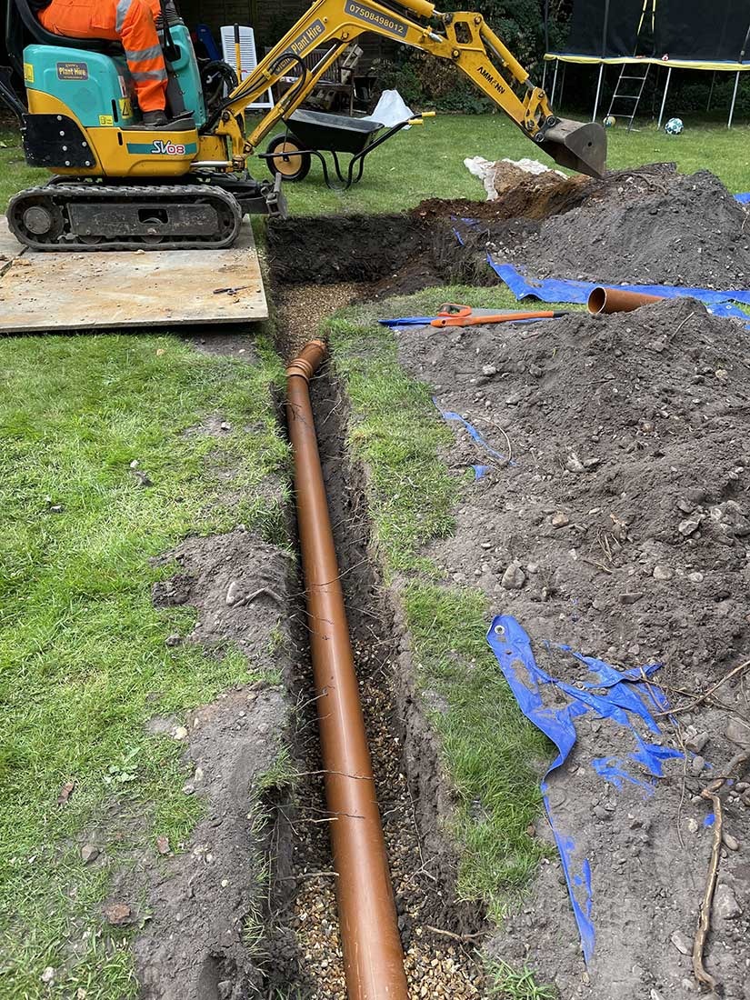 New 110mm orange drainage pipe being laid in a trench by Overflow engineers in Berkshire
