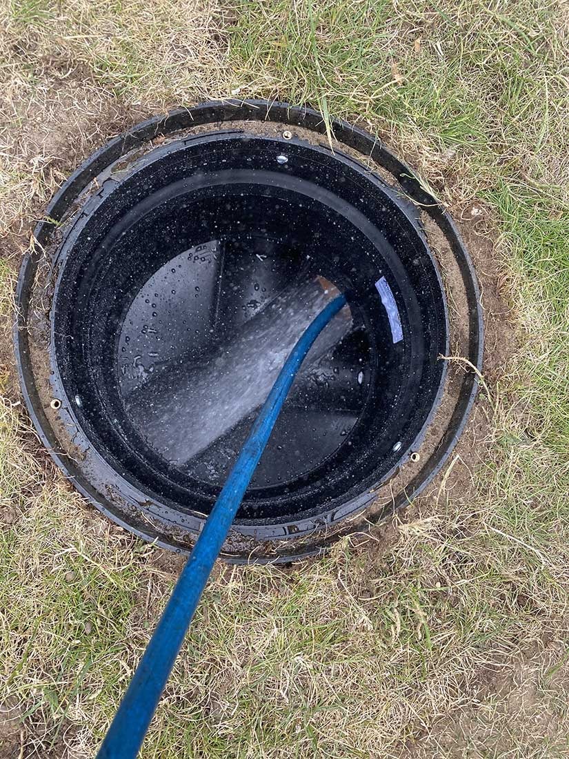 Blue jetting hose clearing a grass-set manhole during a Berkshire drain unblocking job